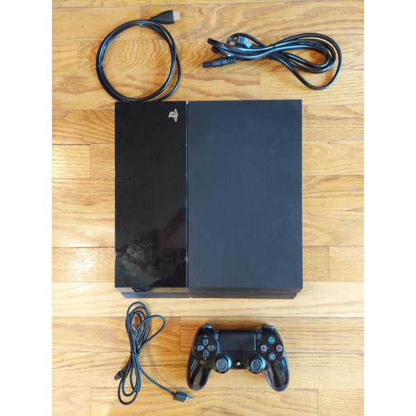 PlayStation 4 gaming console with controller and cables on a wooden surface