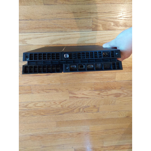 PlayStation 4 gaming console with controller and cables on a wooden surface