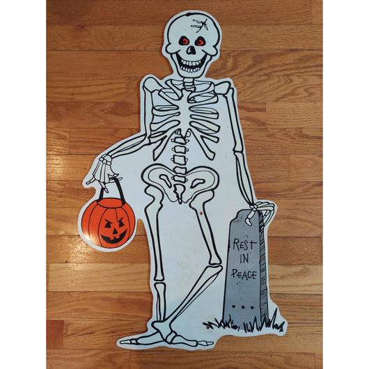 Skeleton cutout with a pumpkin and 'Rest in Peace' sign on a wooden floor